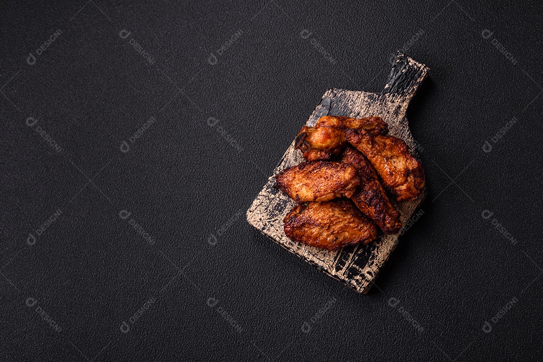 Deliciosas asas de frango suculentas assadas na grelha com sal, especiarias e ervas sobre um fundo escuro de concreto