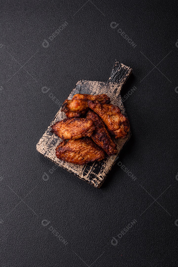 Deliciosas asas de frango suculentas assadas na grelha com sal, especiarias e ervas sobre um fundo escuro de concreto