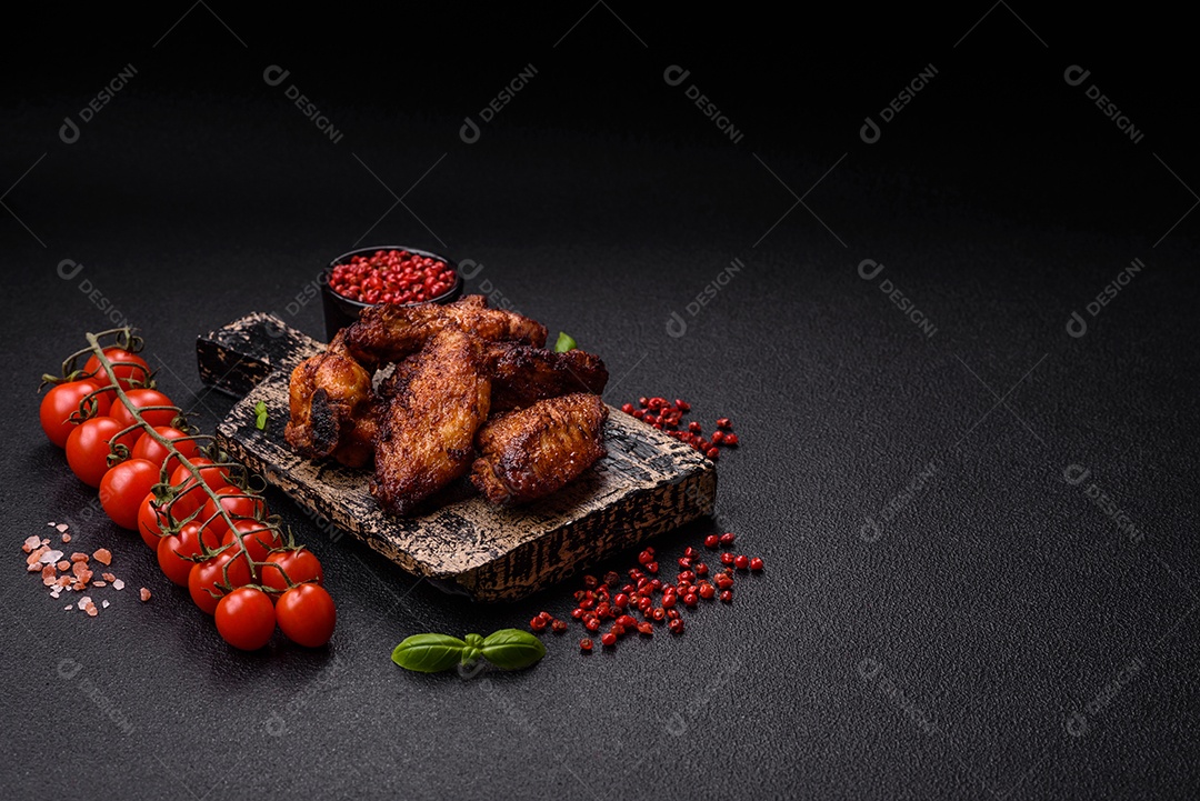 Deliciosas asas de frango suculentas assadas na grelha com sal, especiarias e ervas sobre um fundo escuro de concreto