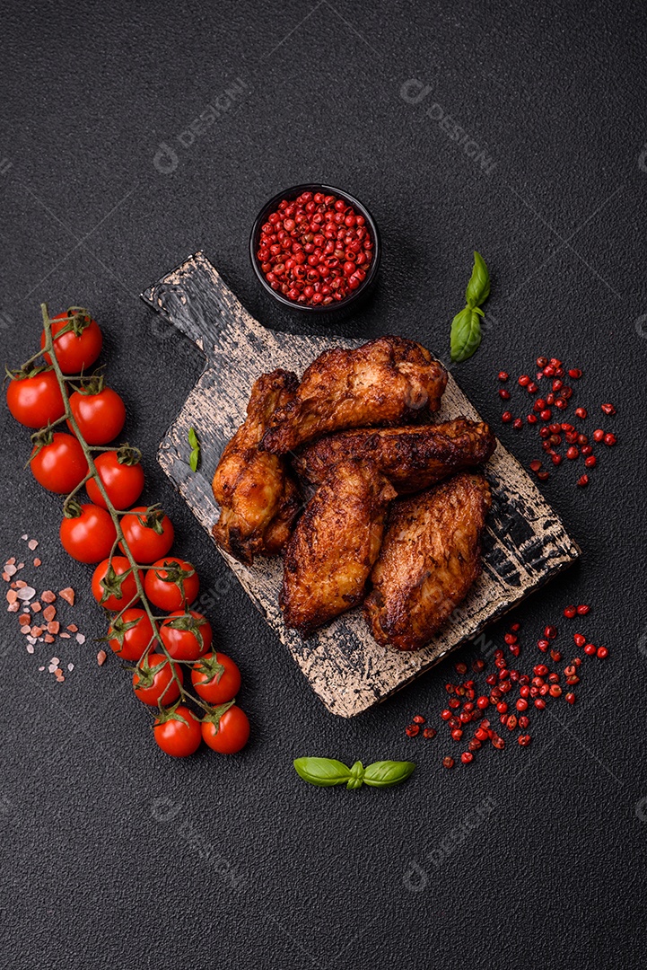 Deliciosas asas de frango suculentas assadas na grelha com sal, especiarias e ervas sobre um fundo escuro de concreto
