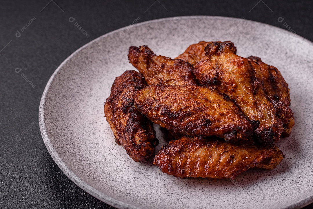 Deliciosas asas de frango suculentas assadas na grelha com sal, especiarias e ervas sobre um fundo escuro de concreto