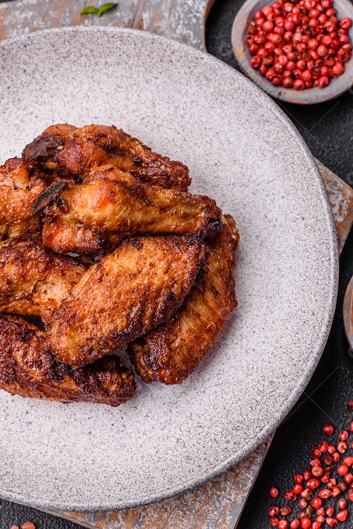 Deliciosas asas de frango suculentas assadas na grelha com sal, especiarias e ervas sobre um fundo escuro de concreto