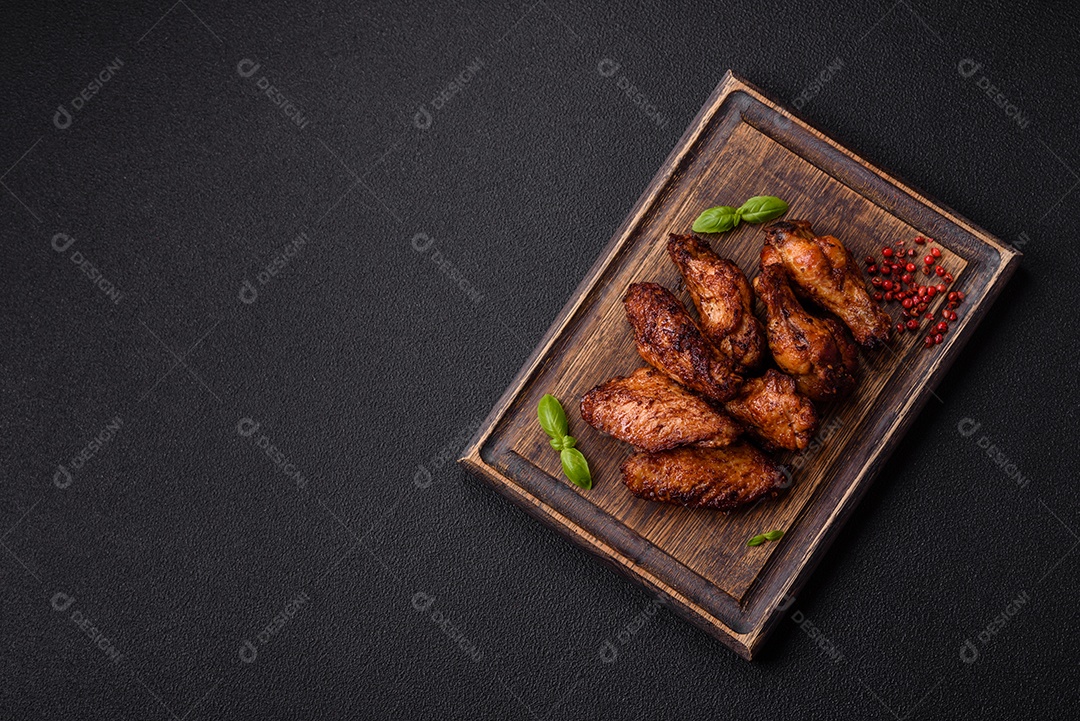 Deliciosas asas de frango suculentas assadas na grelha com sal, especiarias e ervas sobre um fundo escuro de concreto