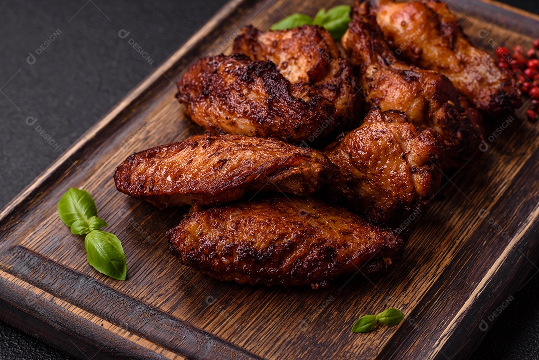 Deliciosas asas de frango suculentas assadas na grelha com sal, especiarias e ervas sobre um fundo escuro de concreto