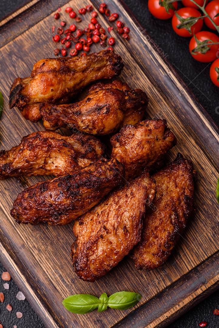 Deliciosas asas de frango suculentas assadas na grelha com sal, especiarias e ervas sobre um fundo escuro de concreto