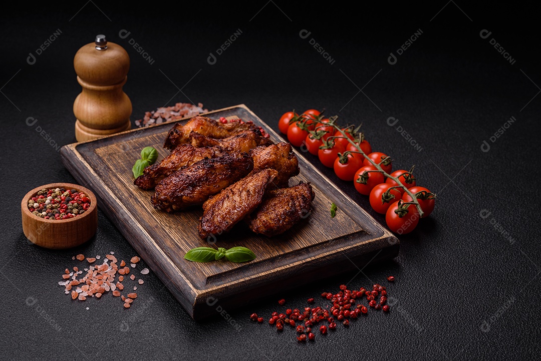 Deliciosas asas de frango suculentas assadas na grelha com sal, especiarias e ervas sobre um fundo escuro de concreto