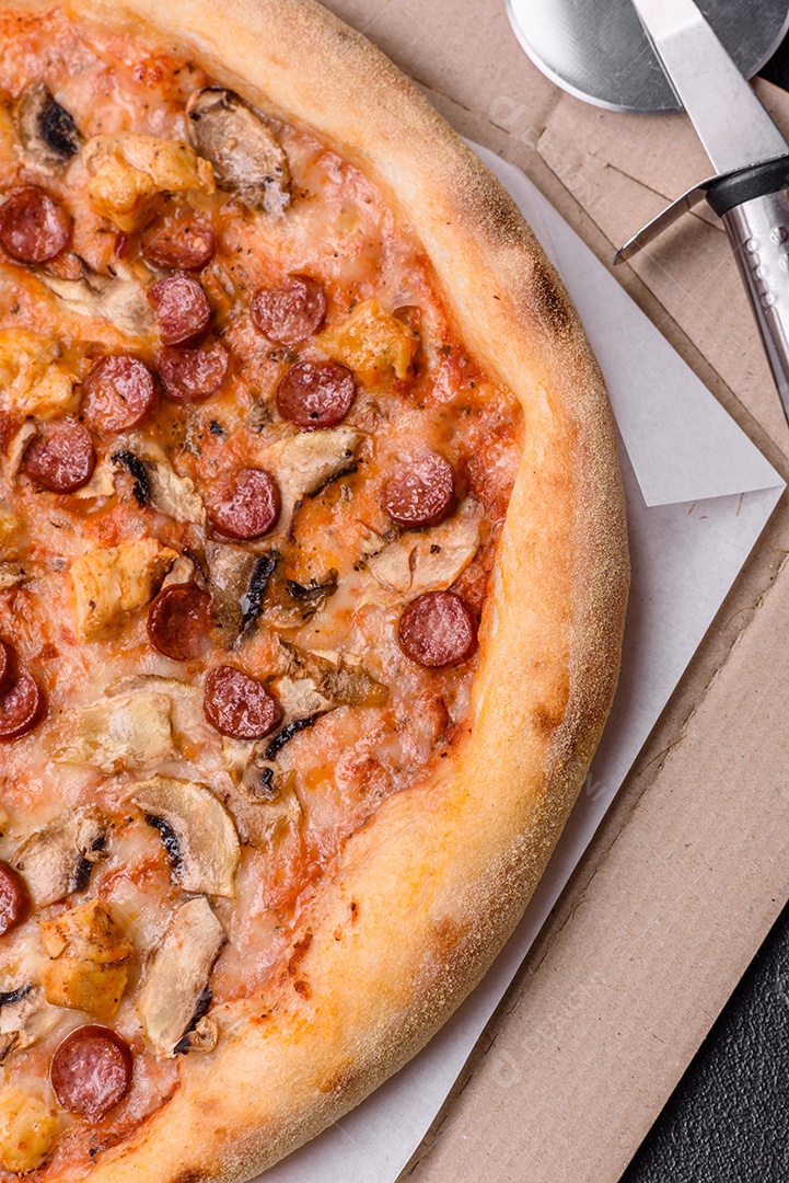 Deliciosa pizza com salsicha, queijo, tomate, sal, especiarias e ervas sobre um fundo escuro de concreto