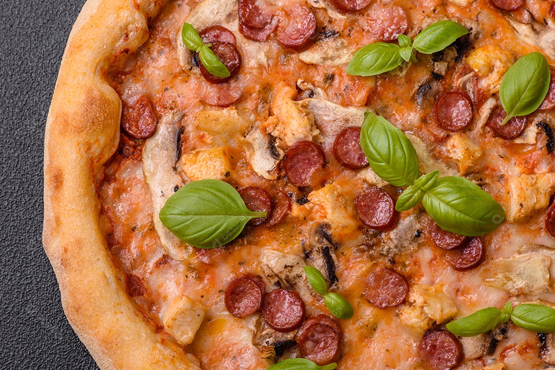 Deliciosa pizza com salsicha, queijo, tomate, sal, especiarias e ervas sobre um fundo escuro de concreto