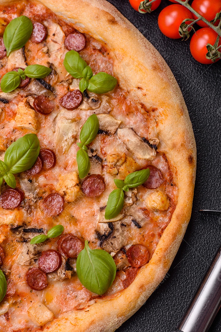 Deliciosa pizza com salsicha, queijo, tomate, sal, especiarias e ervas sobre um fundo escuro de concreto