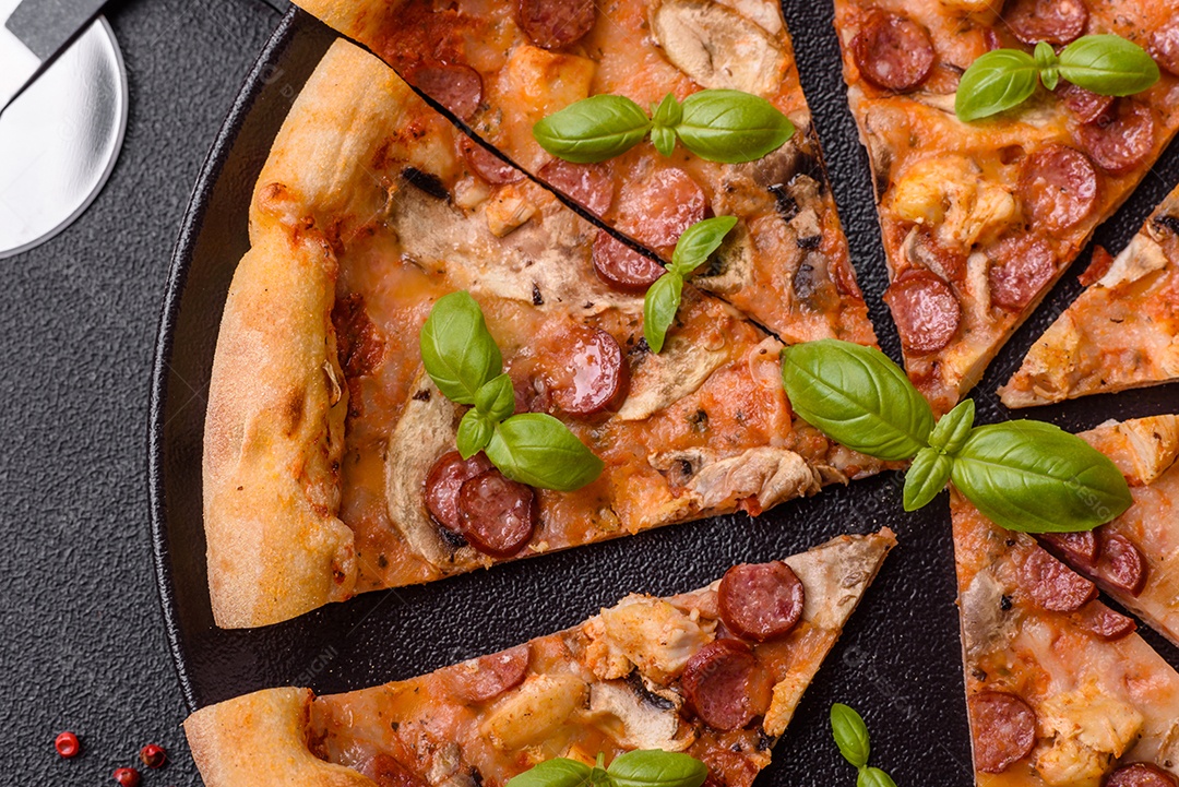 Deliciosa pizza com salsicha, queijo, tomate, sal, especiarias e ervas sobre um fundo escuro de concreto