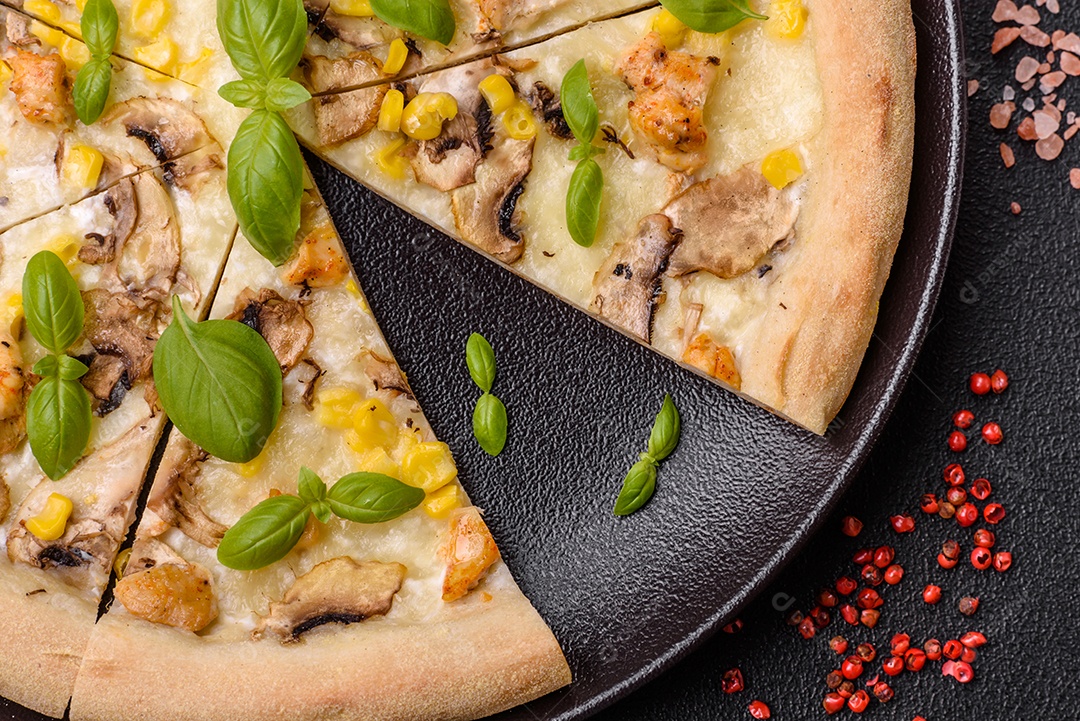 Deliciosa pizza com milho, queijo, tomate e cogumelos, sal, especiarias e ervas sobre fundo escuro de concreto