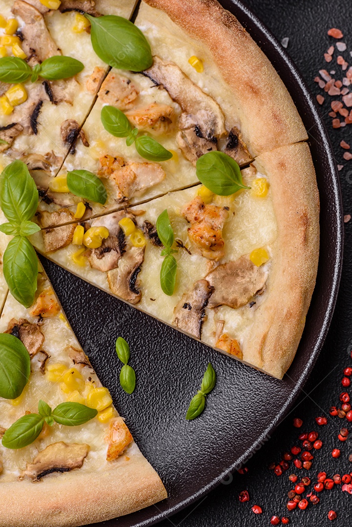 Deliciosa pizza com milho, queijo, tomate e cogumelos, sal, especiarias e ervas sobre fundo escuro de concreto