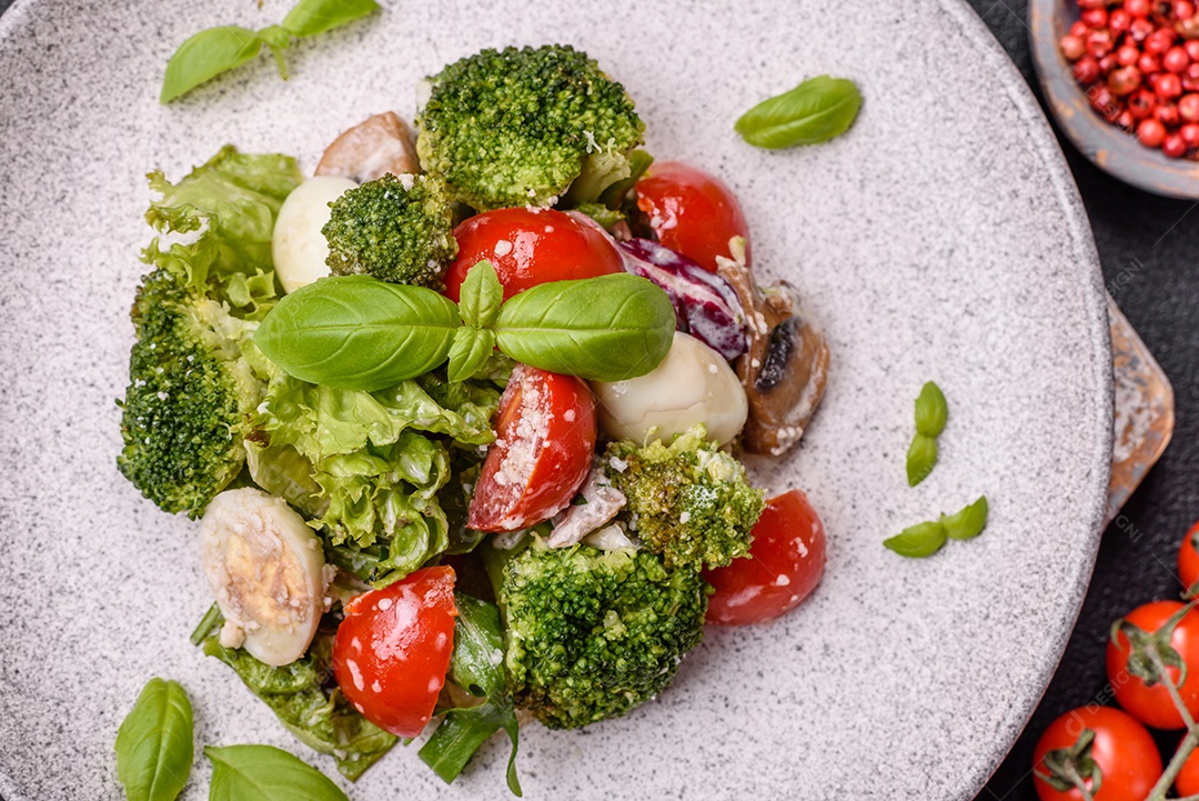 Deliciosa salada fresca e suculenta com ovos de codorna, tomate cereja, folhas de alface com sal, especiarias e ervas sobre um fundo escuro de concreto