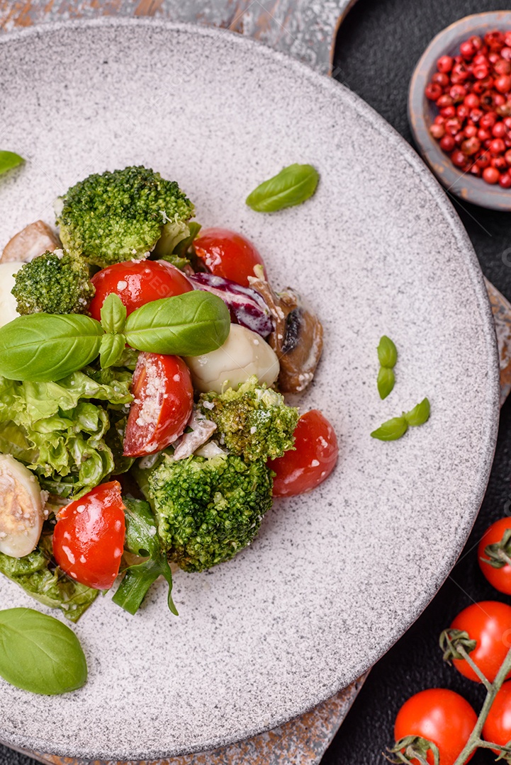 Deliciosa salada fresca e suculenta com ovos de codorna, tomate cereja, folhas de alface com sal, especiarias e ervas sobre um fundo escuro de concreto