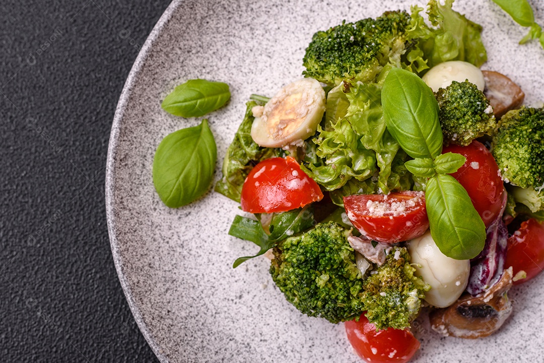 Deliciosa salada fresca e suculenta com ovos de codorna, tomate cereja, folhas de alface com sal, especiarias e ervas sobre um fundo escuro de concreto