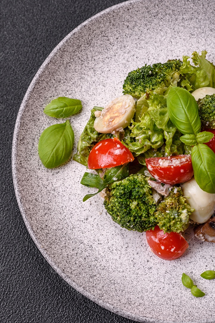 Deliciosa salada fresca e suculenta com ovos de codorna, tomate cereja, folhas de alface com sal, especiarias e ervas sobre um fundo escuro de concreto