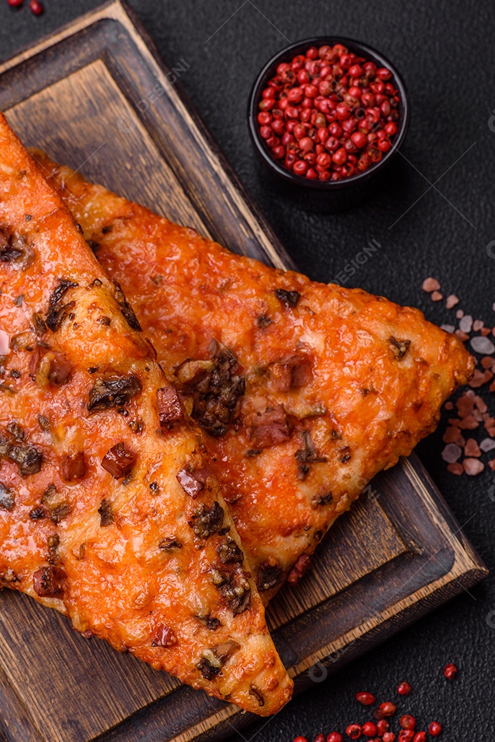 Fatias de deliciosa pizza de rua com salsicha, cogumelos, tomate e queijo com sal e especiarias sobre um fundo escuro de concreto