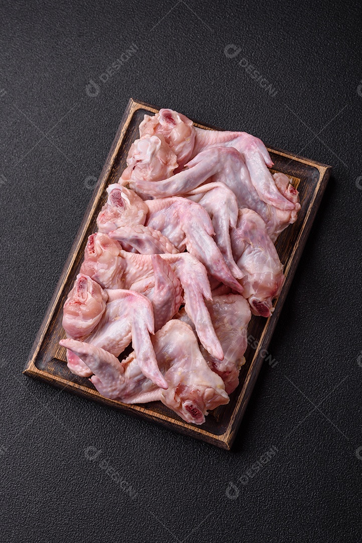 Asas de frango fresco com sal, especiarias e ervas sobre um fundo escuro de concreto