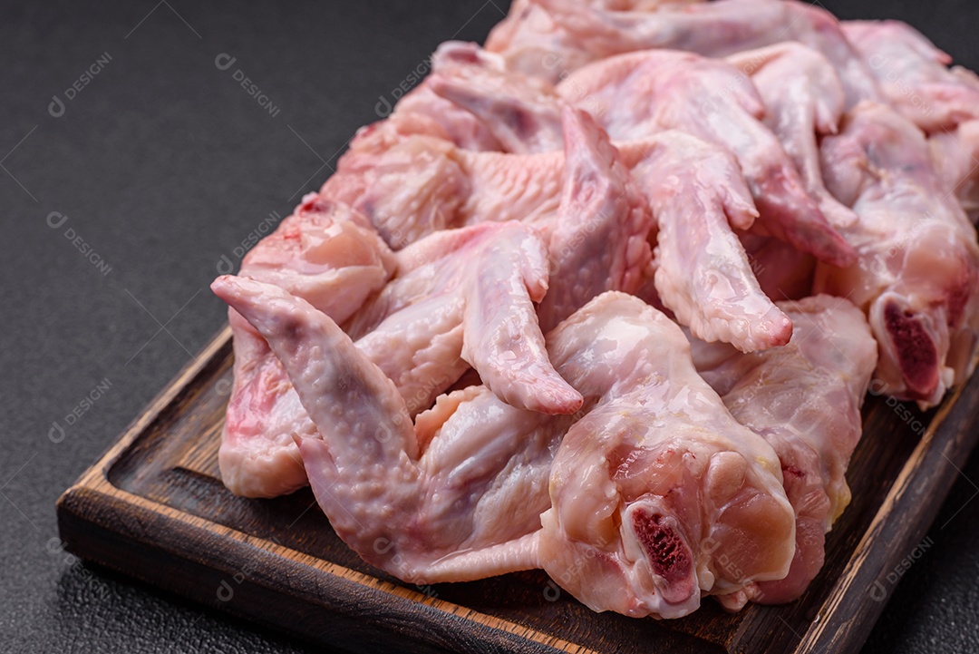 Asas de frango fresco com sal, especiarias e ervas sobre um fundo escuro de concreto