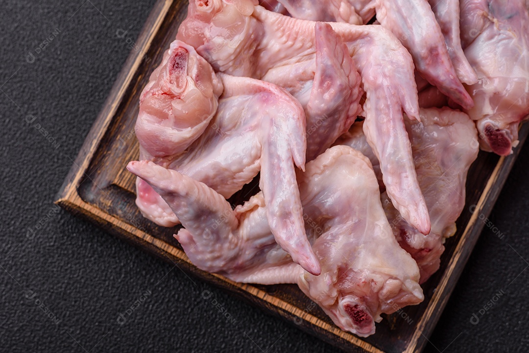 Asas de frango fresco com sal, especiarias e ervas sobre um fundo escuro de concreto