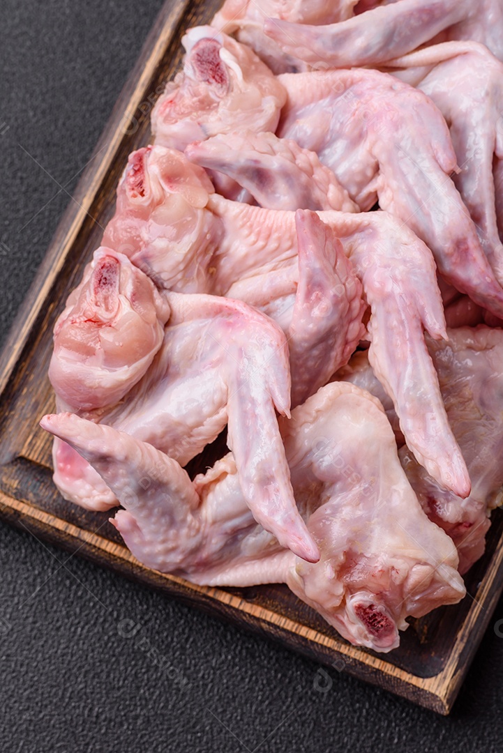 Asas de frango fresco com sal, especiarias e ervas sobre um fundo escuro de concreto