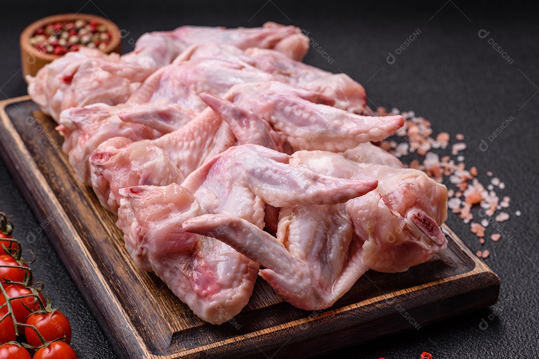 Asas de frango fresco com sal, especiarias e ervas sobre um fundo escuro de concreto