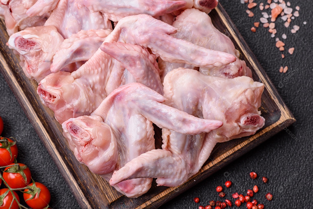 Asas de frango fresco com sal, especiarias e ervas sobre um fundo escuro de concreto