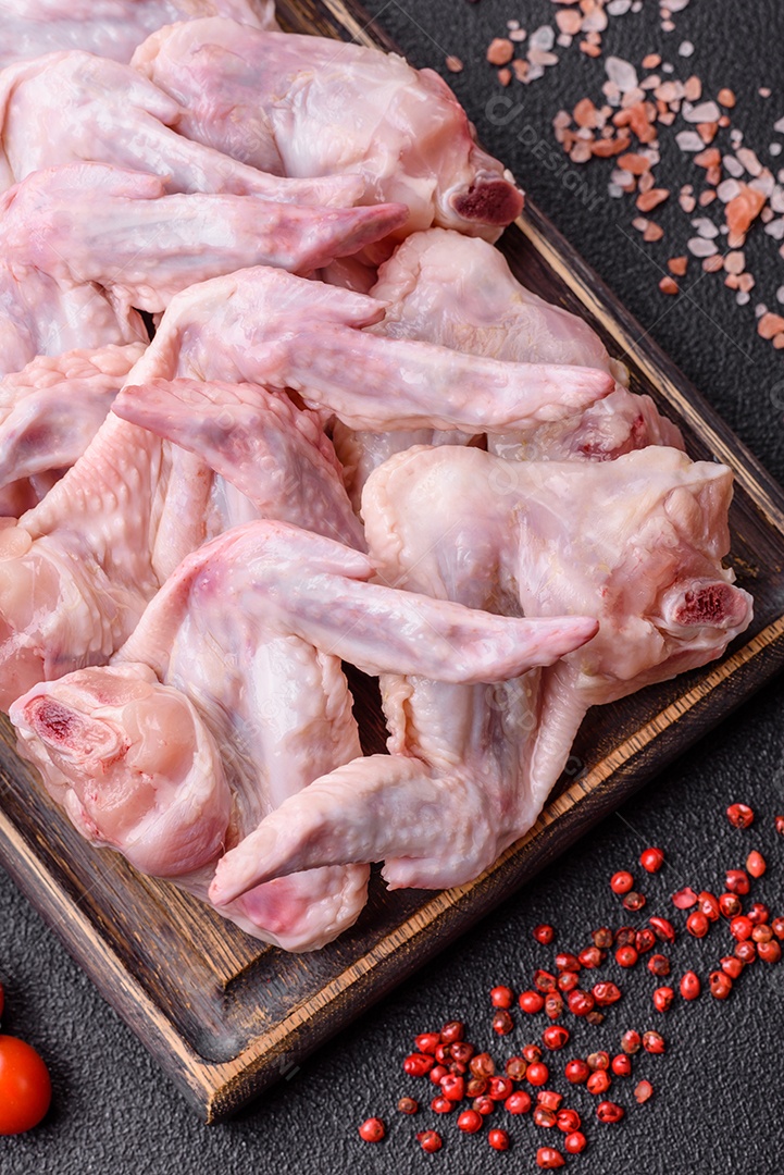 Asas de frango fresco com sal, especiarias e ervas sobre um fundo escuro de concreto