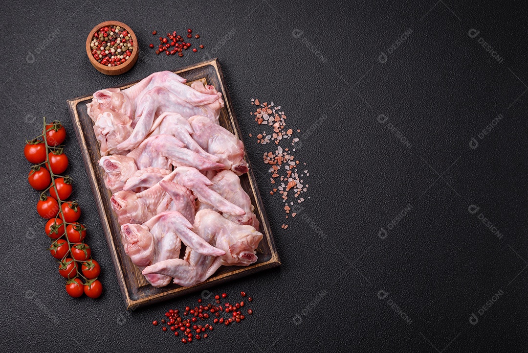 Asas de frango fresco com sal, especiarias e ervas sobre um fundo escuro de concreto