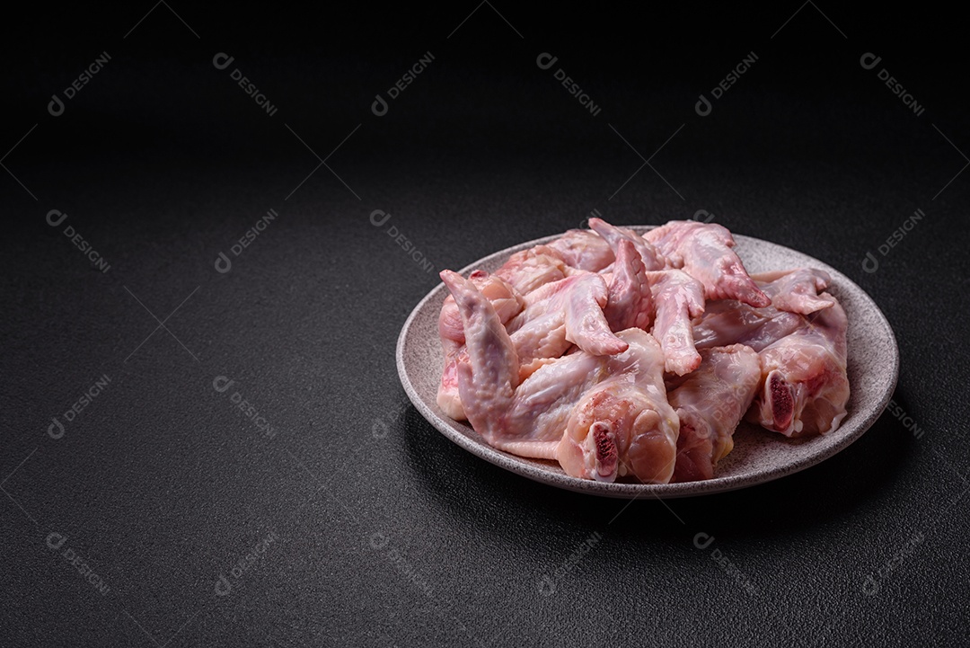 Asas de frango fresco com sal, especiarias e ervas sobre um fundo escuro de concreto