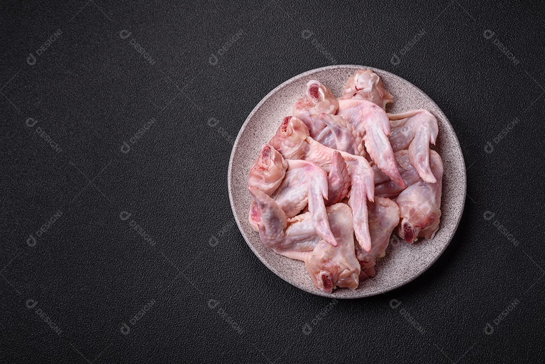 Asas de frango fresco com sal, especiarias e ervas sobre um fundo escuro de concreto