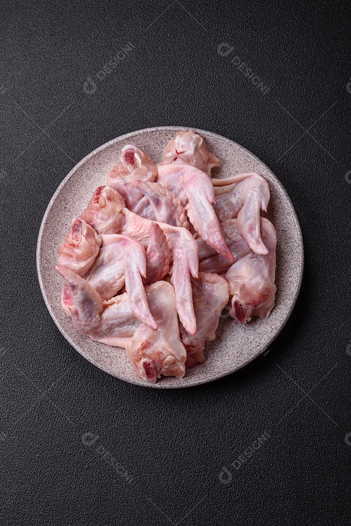 Asas de frango fresco com sal, especiarias e ervas sobre um fundo escuro de concreto