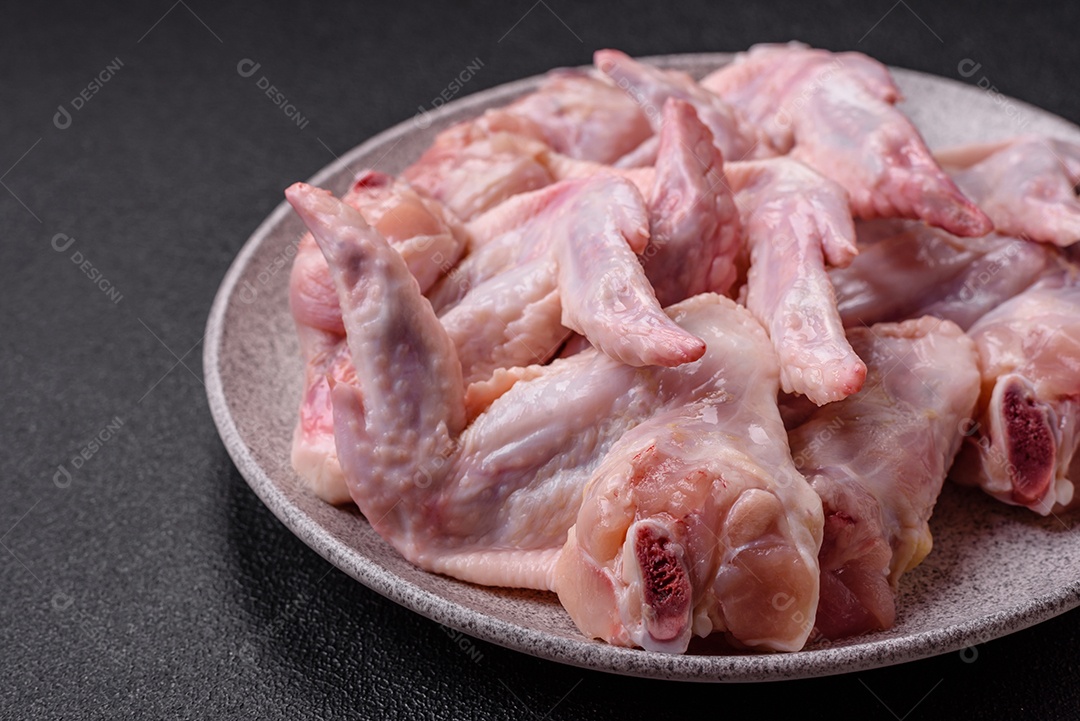 Asas de frango fresco com sal, especiarias e ervas sobre um fundo escuro de concreto
