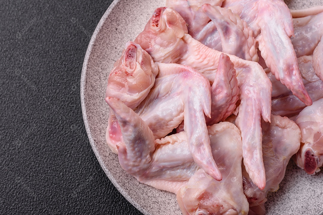 Asas de frango fresco com sal, especiarias e ervas sobre um fundo escuro de concreto