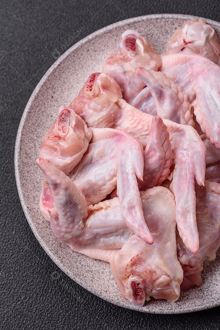 Asas de frango fresco com sal, especiarias e ervas sobre um fundo escuro de concreto