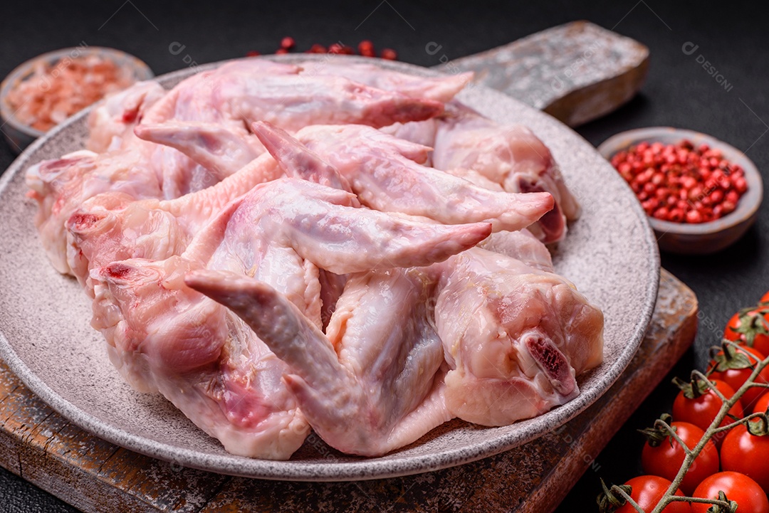 Asas de frango fresco com sal, especiarias e ervas sobre um fundo escuro de concreto