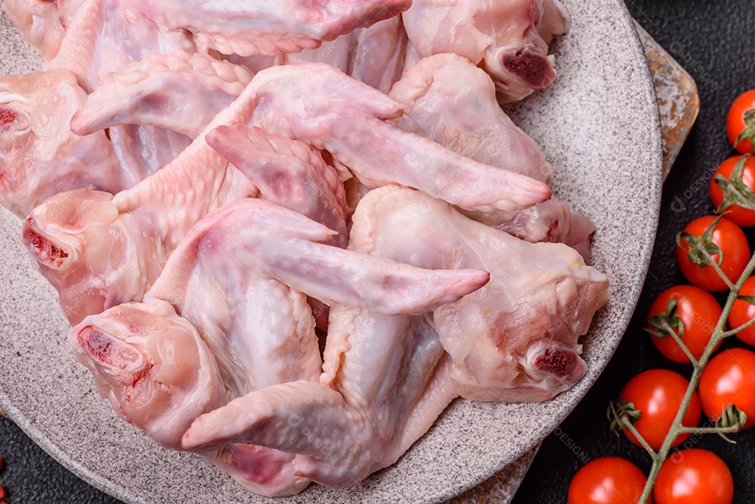 Asas de frango fresco com sal, especiarias e ervas sobre um fundo escuro de concreto