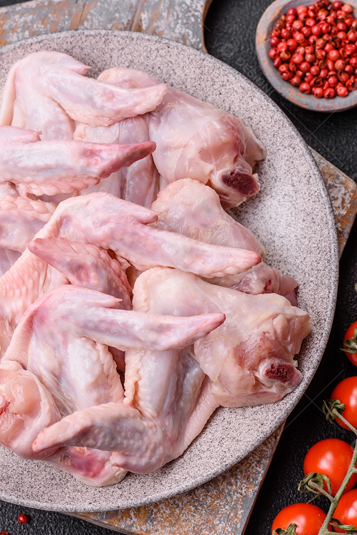 Asas de frango fresco com sal, especiarias e ervas sobre um fundo escuro de concreto