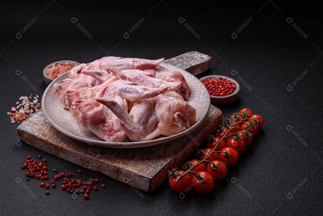 Asas de frango fresco com sal, especiarias e ervas sobre um fundo escuro de concreto