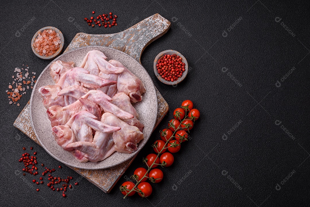 Asas de frango fresco com sal, especiarias e ervas sobre um fundo escuro de concreto