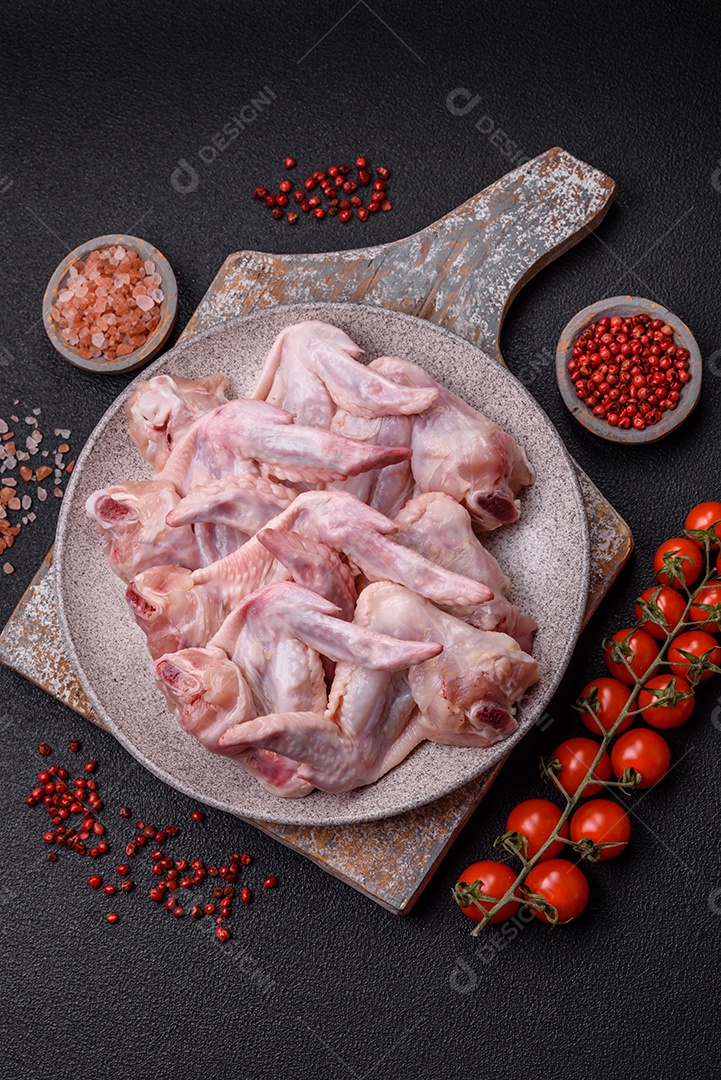 Asas de frango fresco com sal, especiarias e ervas sobre um fundo escuro de concreto