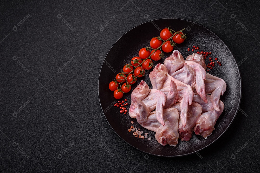 Asas de frango fresco com sal, especiarias e ervas sobre um fundo escuro de concreto