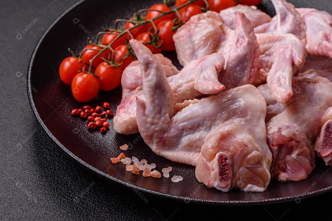 Asas de frango fresco com sal, especiarias e ervas sobre um fundo escuro de concreto