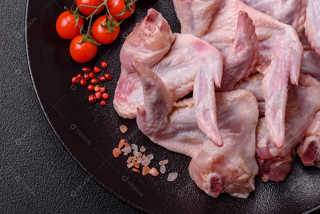 Asas de frango fresco com sal, especiarias e ervas sobre um fundo escuro de concreto