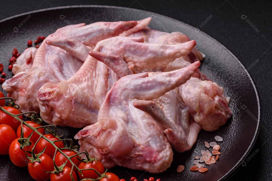 Asas de frango fresco com sal, especiarias e ervas sobre um fundo escuro de concreto