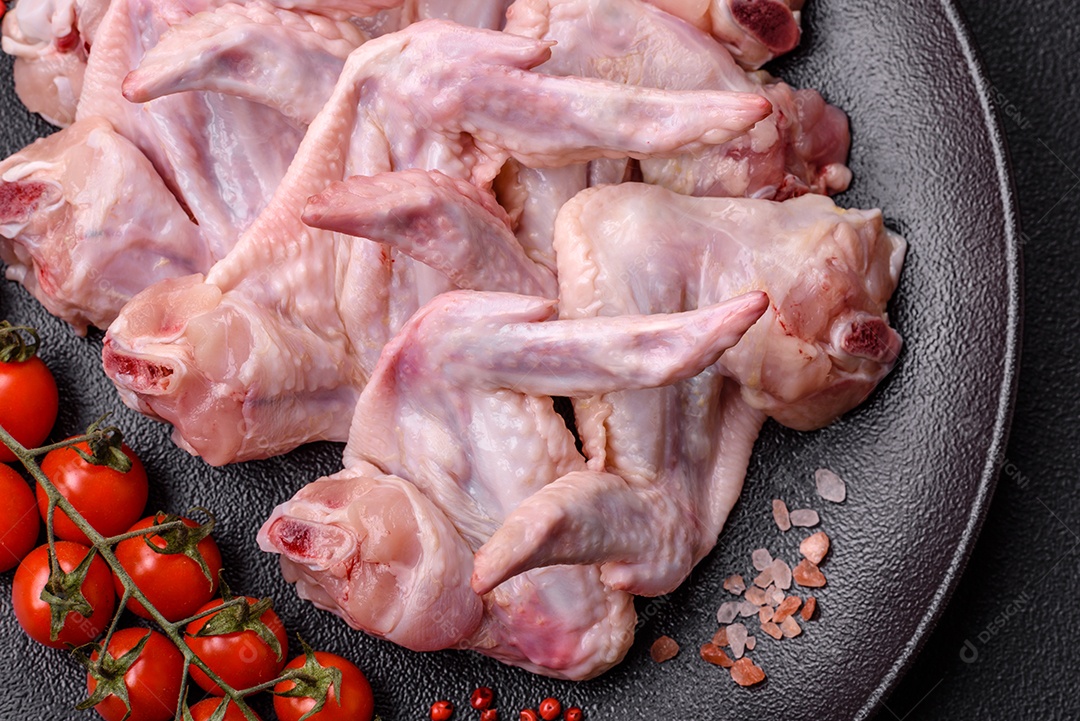 Asas de frango fresco com sal, especiarias e ervas sobre um fundo escuro de concreto