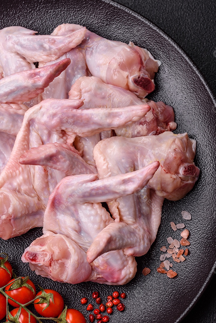 Asas de frango fresco com sal, especiarias e ervas sobre um fundo escuro de concreto