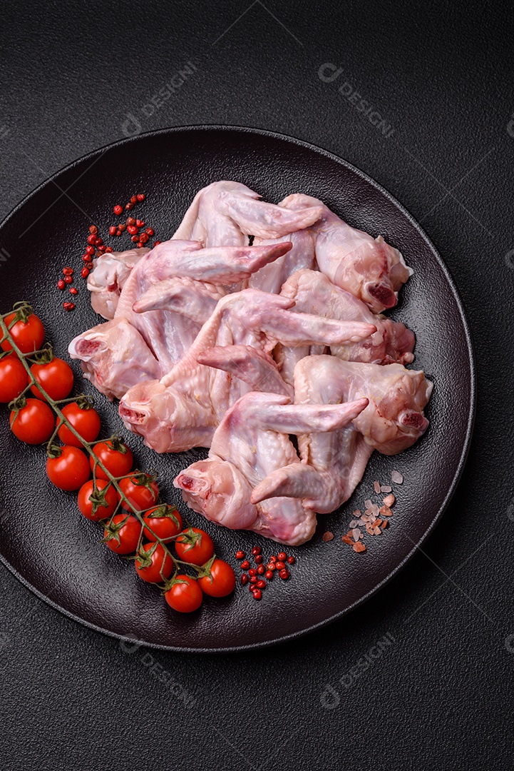 Asas de frango fresco com sal, especiarias e ervas sobre um fundo escuro de concreto