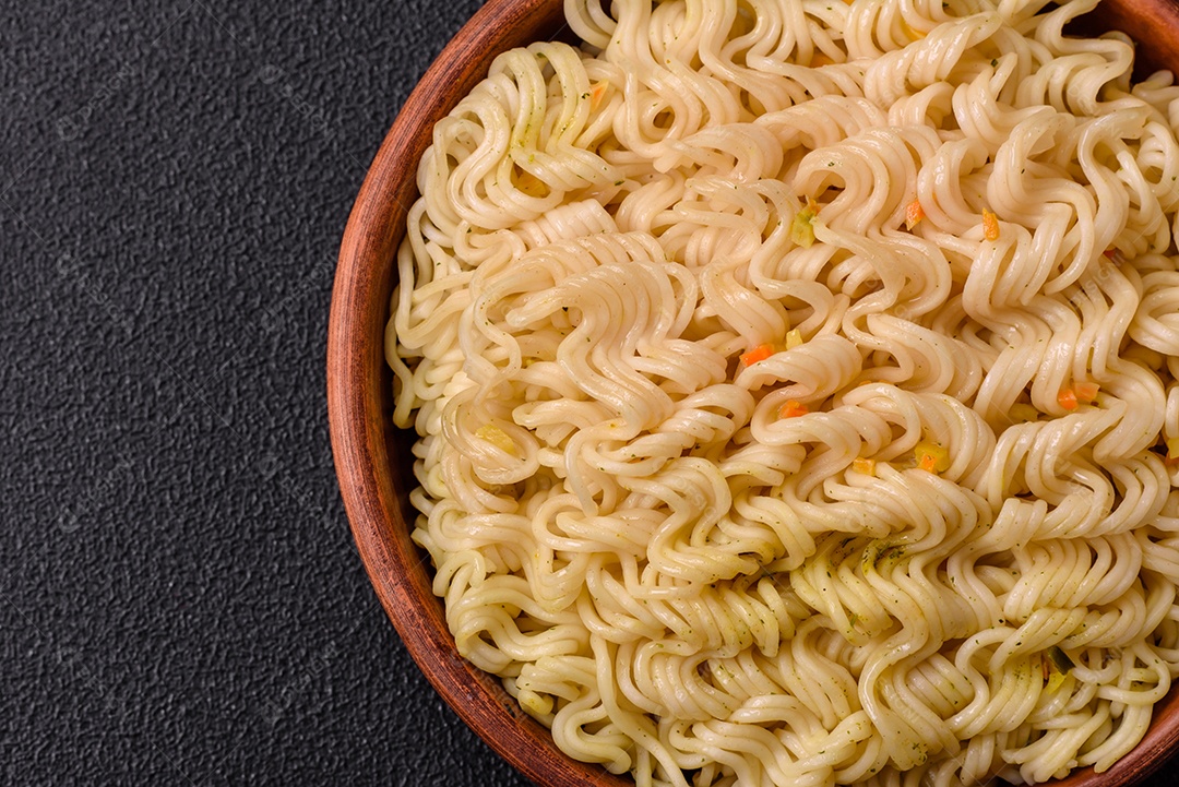 Delicioso macarrão de arroz asiático ou udon com legumes, especiarias e ervas sobre um fundo escuro de concreto