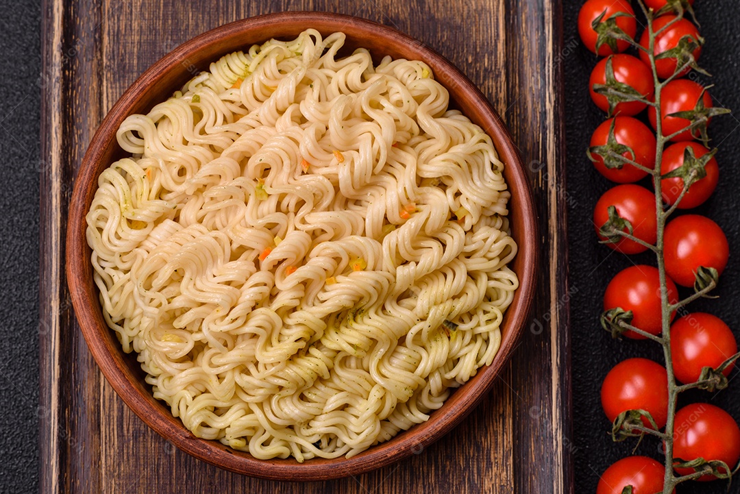 Delicioso macarrão de arroz asiático ou udon com legumes, especiarias e ervas sobre um fundo escuro de concreto